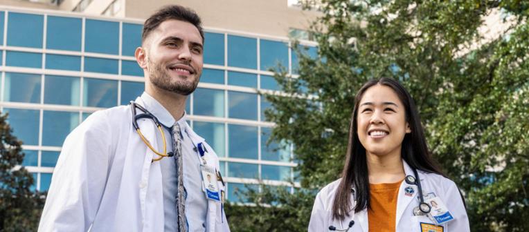 Two students in white coats standing in front of Ochsner building