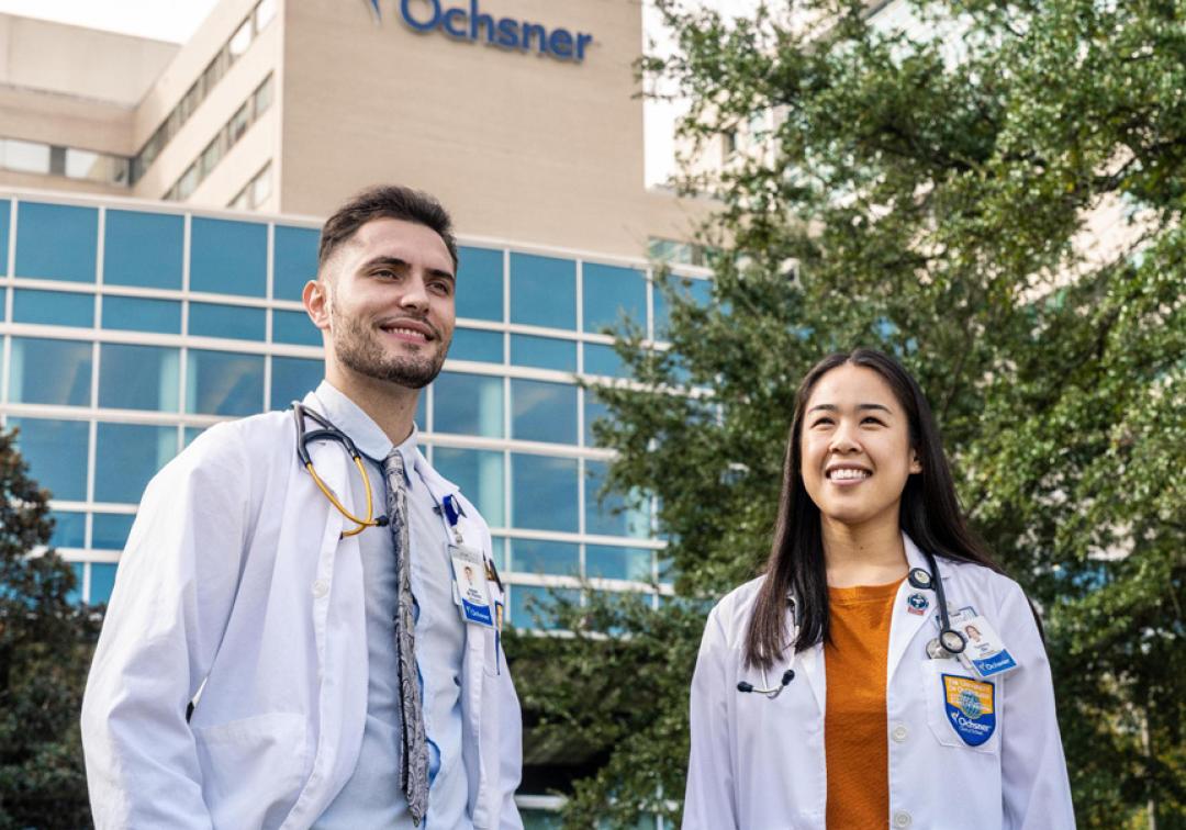 Two students in white coats standing in front of Ochsner building