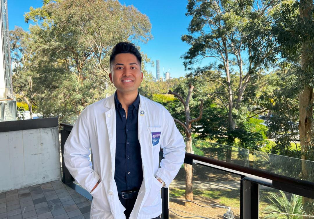 UQ-Ochsner medical student, Brian Gutierrez wearing a white coat with the Brisbane skyline in the background.