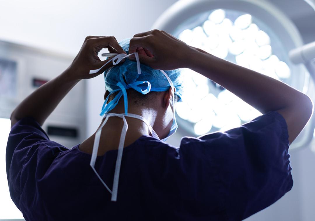 A surgeon ties up the straps of their surgical mask. 