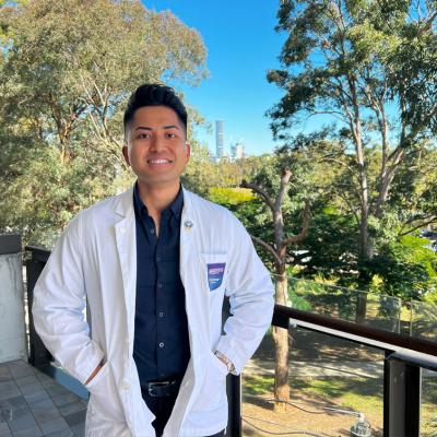 UQ-Ochsner medical student, Brian Gutierrez wearing a white coat with the Brisbane skyline in the background.