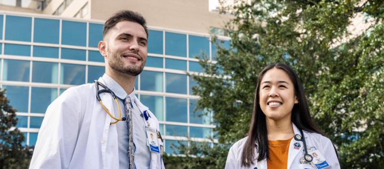 Two students in white coats standing in front of Ochsner building