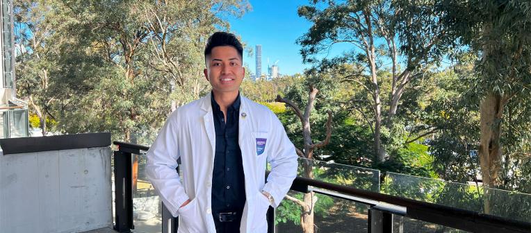 UQ-Ochsner medical student, Brian Guttierez, wearing a white coat with the Brisbane skyline in the background.