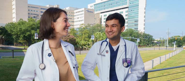 A female and male UQ-Ochnser medical student chatting with an Ochsner Health hospital in the background